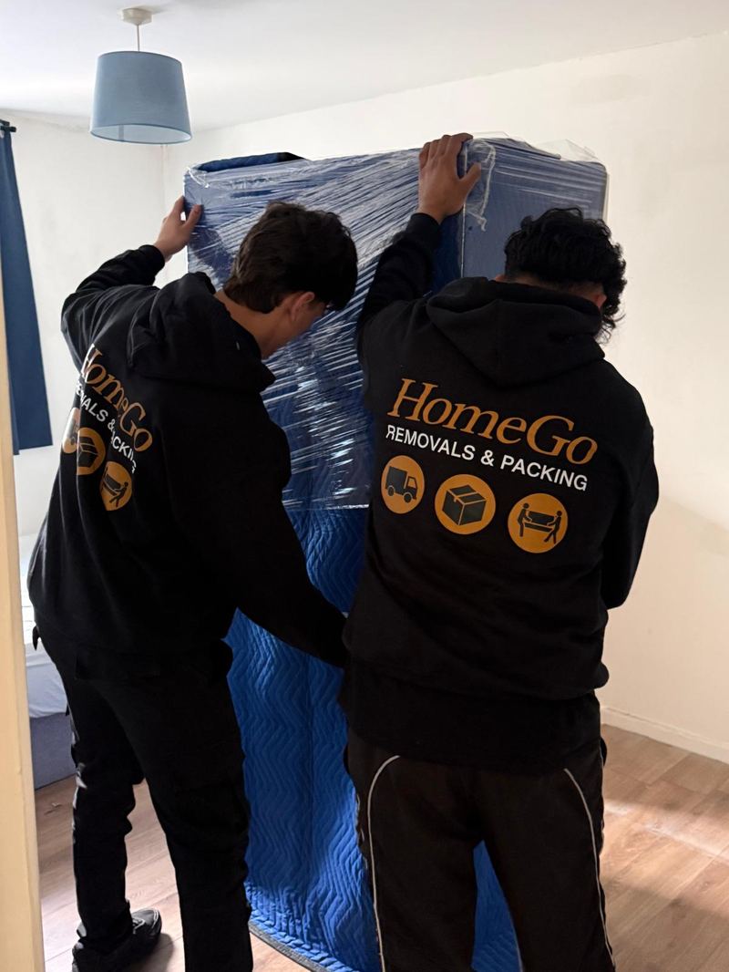 HomeGo Removals crew transporting a fully-wrapped item on a professional trolley outside a heritage building in the UK
